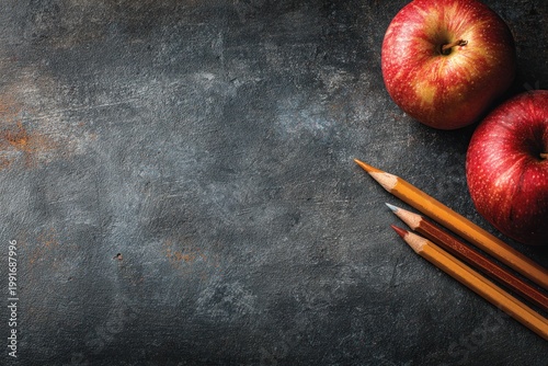 Red apples and pencils on dark textured slate background