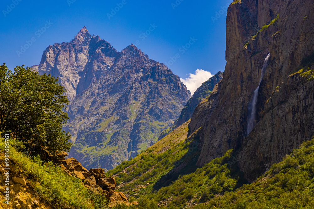 Fototapeta premium Majestic mountain peaks with waterfall and greenery