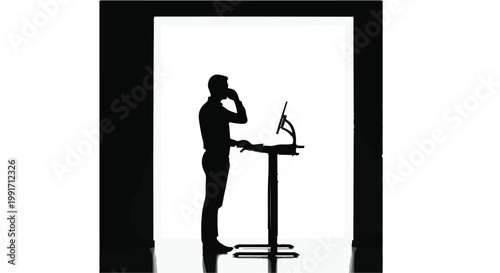 Silhouette of a businessman using a standing desk while talking on a phone.