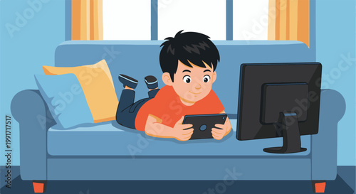 A boy lies on a couch playing a tablet game, a computer monitor nearby