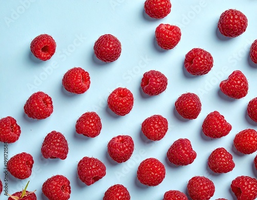 Bright red raspberries scattered on a pale blue surface