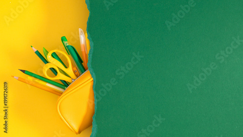 Back to school concept with yellow pencil case full of stationery under torn green paper on yellow background, minimalist creative flat lay with copy space for text, education and study banner.