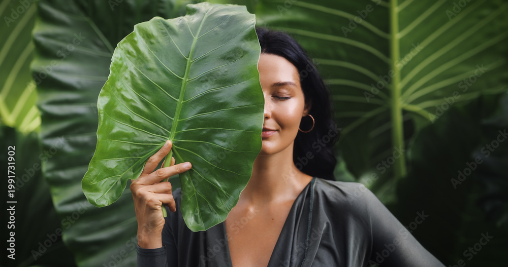 Naklejka premium Radiant Tanned Woman With Leaf Covering Face, Natural Skincare Portrait