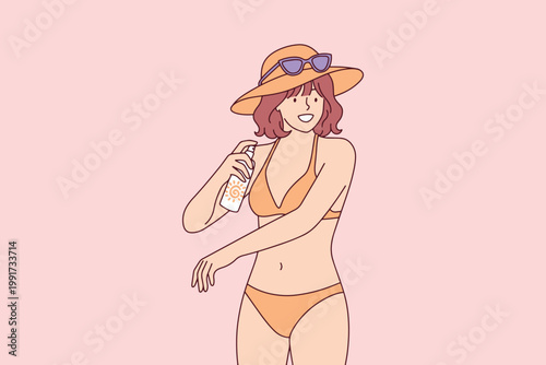 Young woman in swimsuit and straw hat applying protective aerosol sunscreen on skin. Sunny beach day concept for summer vacation and skincare.