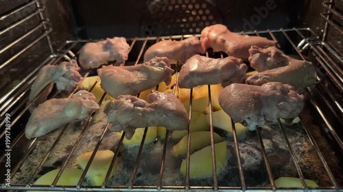 Raw Chicken Wings On Oven Rack With Potato Wedges Below In Warm Oven Light, Home Cook Prepping Family Dinner,