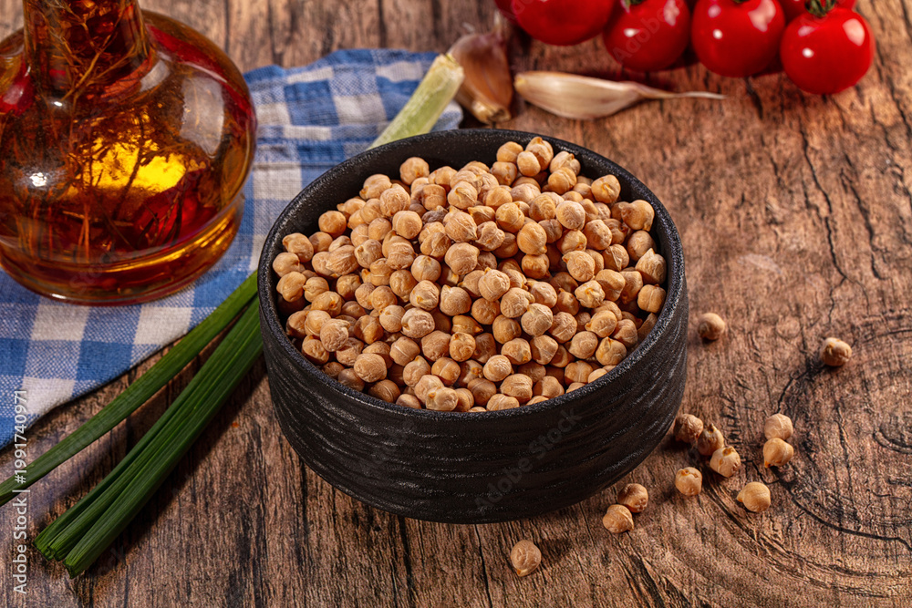 Fototapeta premium Dry chickpeas in black bowl with fresh ingredients on rustic wood