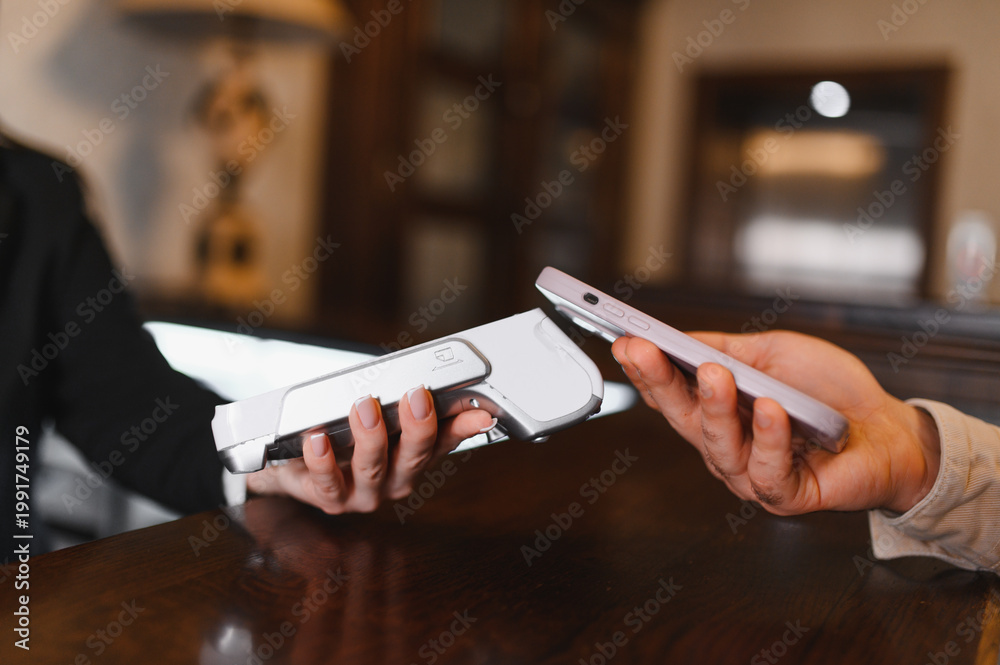 Obraz premium Customer making contactless mobile payment at hotel reception desk