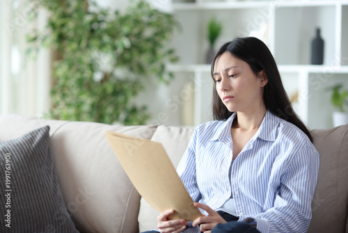 Worried asian woman checking paper documents at home