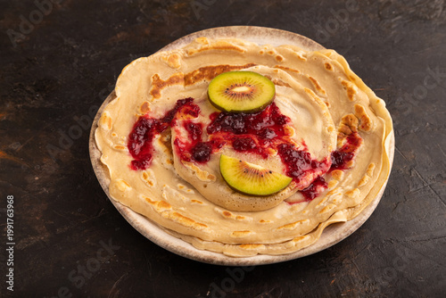 Stack of Plain Fried pancakes with jam and kiwi on black concrete. side view, close up