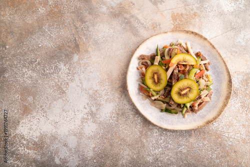 Meat salad with beef, kiwi and vegetables on brown concrete, top view, copy space