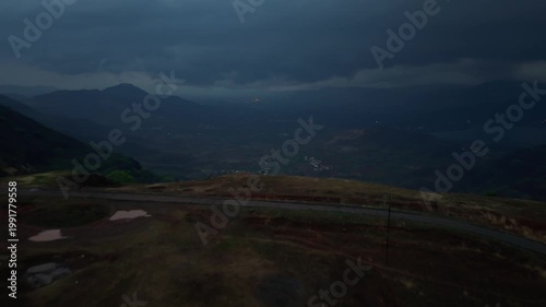 Moving drone shot of dark monsoon clouds over a valley with mountain top in the foreground shot after sunset. Dramatic scene. 4K30fps