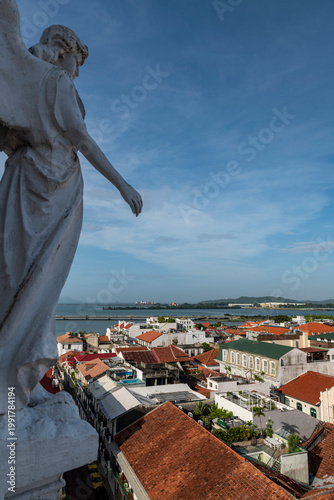 Angel statue of San Francisco church providing a high-angle view over the red tiled rooftops of casco viejo, showing the scenic urban landscape and the bay of Panama on a clear day - stock photo