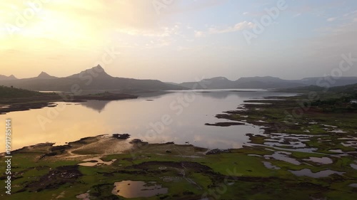 Moving drone shot of Sunset over a lake with dramatic clouds and Mountains in the background shot during monsoon. 4K60fps