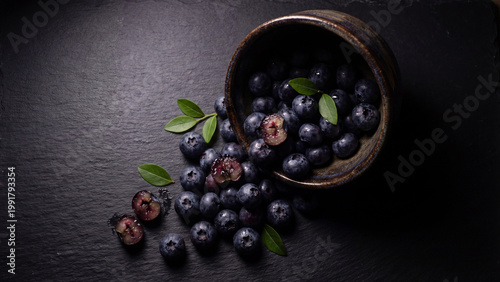 Blueberry bowl spilled on dark surface with fresh ripe berries and leaves