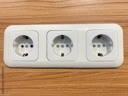 Triple white wall power outlet installed on wooden surface background