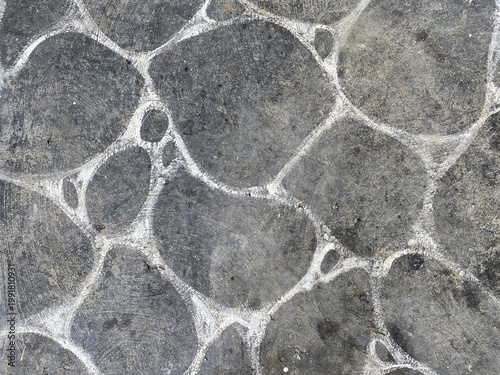Close-up of irregular stone pavement with textured concrete and white grout lines.
