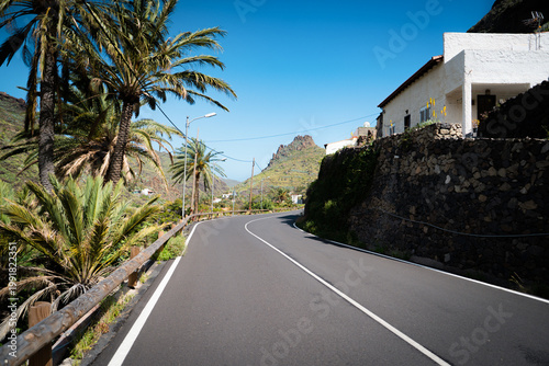 Scenic empty road surrounded by tropical vegetation, palm trees and mountains. Ideal for travel, road trip, freedom and adventure concepts.