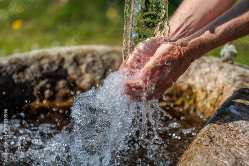 Hands catching fresh flowing spring water from a natural source outdoors, clear splashing stream in sunlight, symbolizing purity, hydration, and clean drinking water