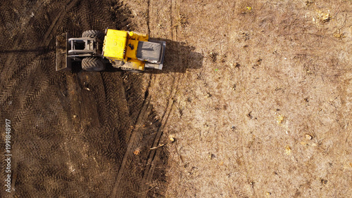A high-angle aerial photograph of a classic yellow heavy-duty tractor equipped with a front loader bucket is Clearing Dirt at Construction Site