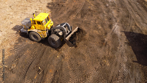 A high-angle aerial photograph of a classic yellow heavy-duty tractor equipped with a front loader bucket is Clearing Dirt at Construction Site