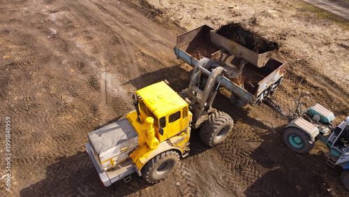 A high-angle aerial photograph of a classic yellow heavy-duty tractor equipped with a front loader bucket is Clearing Dirt at Construction Site