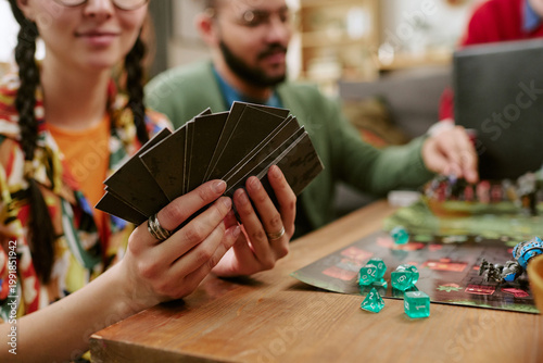 Canvas Print Close up of young adult woman holding game cards while friends playing tabletop
