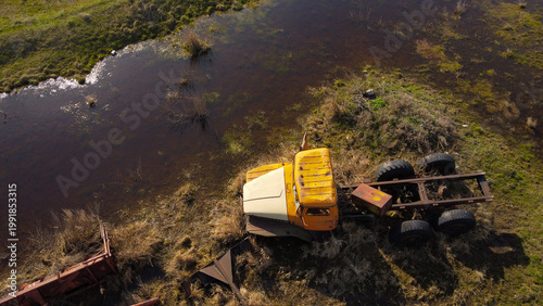 aerial shot of an old, rusted orange and white heavy-duty truck cabin and chassis abandoned in a swampy, waterlogged field