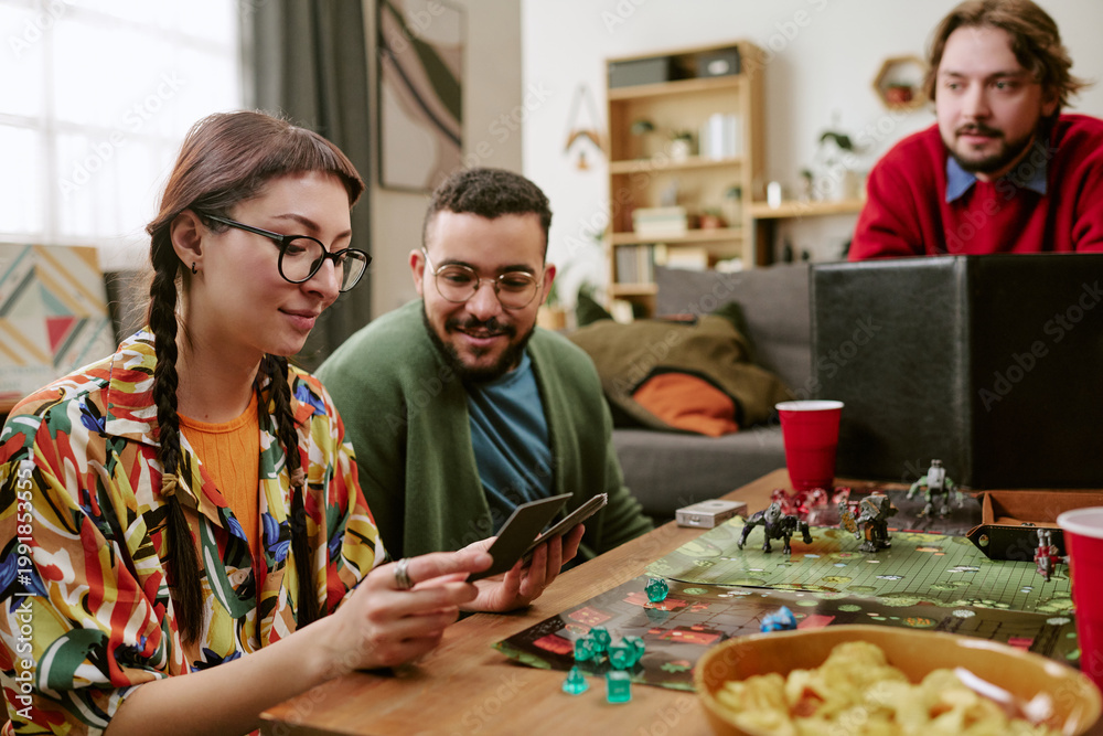 Fototapeta premium Young adult friends playing tabletop role playing game, reading cards and planning moves at home
