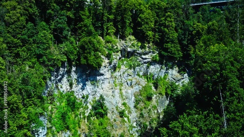 Cinematic aerial reveal from a rocky forest cliff to the picturesque town of Chamonix, France, nestled in the French Alps under a dramatic sky