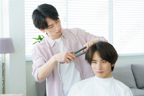 Fotografie ヘアアイロンで髪をカールする若い日本人美容師