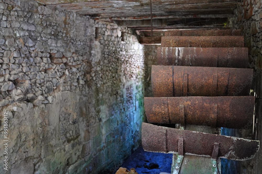 Fototapeta premium Close view of rusty water wheel blades in abandoned stone mill interior France