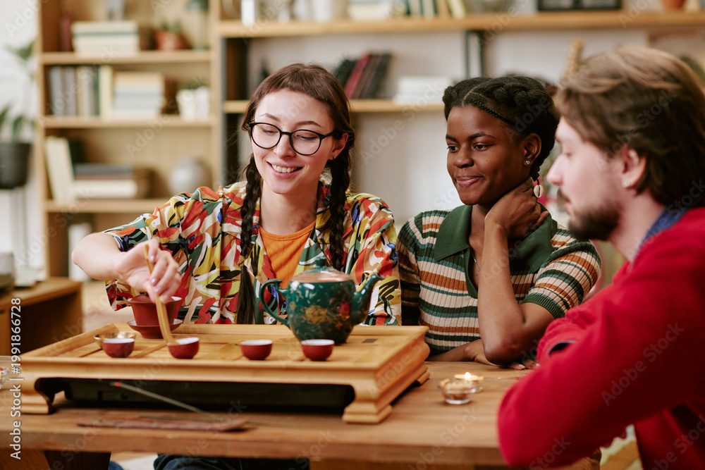 Fototapeta premium Young adult diverse friends preparing tea and sharing cultural ritual at table, demonstrating social connection and leisure