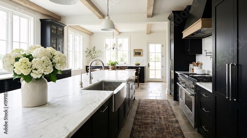 Spacious farmhouse kitchen featuring a massive white marble island, a stainless steel sink, black cabinetry, and fresh white hydrangeas.
