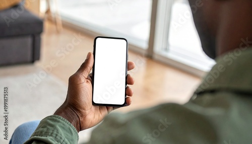 A person holds a smartphone with a blank screen, seen from over the shoulder, indoors
