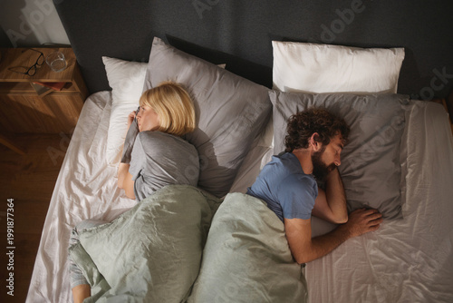 Fotografie A couple lies in separate positions on their bed, showing a clear emotional distance