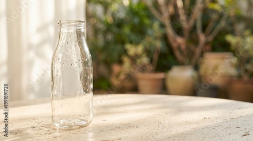 A clear glass bottle sits on a table in a garden with potted plants.
