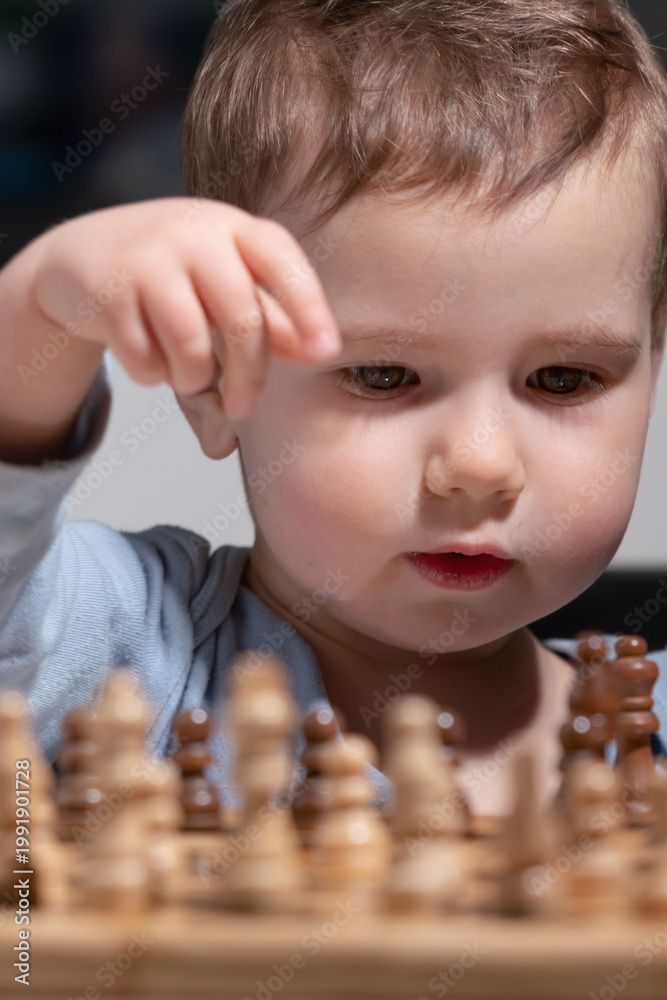 Fototapeta premium Toddler interacting with wooden chess set, symbol of early intellectual development.