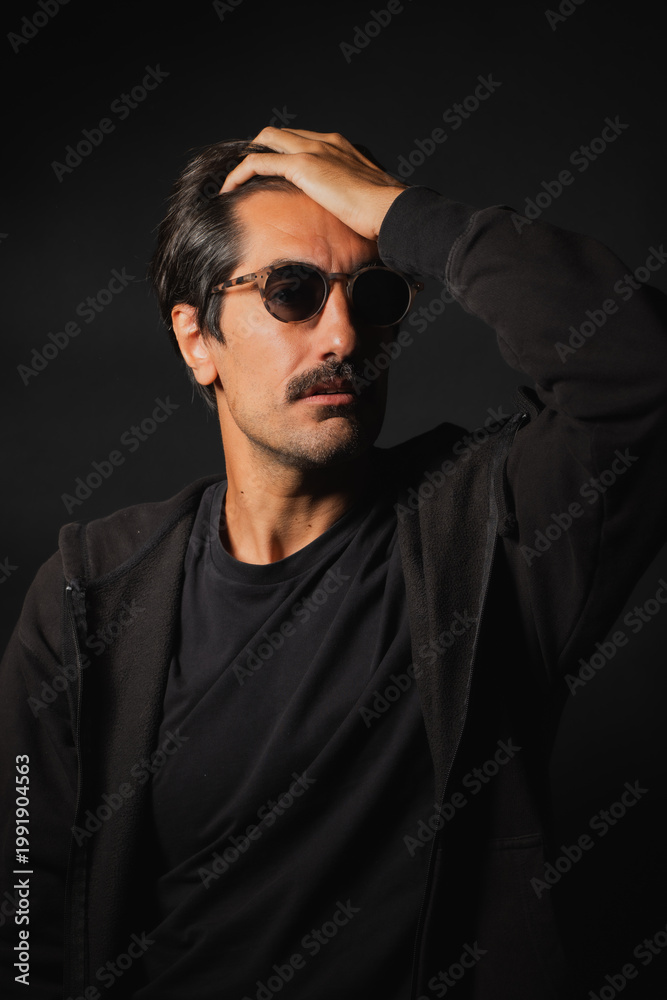 Fototapeta premium Stylish man in sunglasses poses thoughtfully in studio light