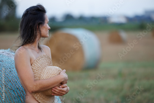 Young woman in countryside holding straw hat, natural summer portrait with hay bales