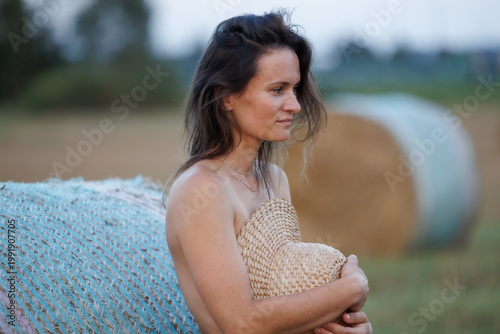 Young woman in countryside holding straw hat, natural summer portrait with hay bales