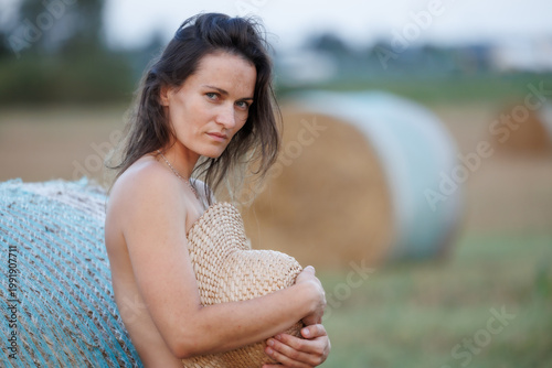 Young woman in countryside holding straw hat, natural summer portrait with hay bales