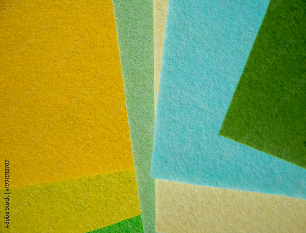 Fototapeta premium Multiple colorful felt fabric sheets in green, yellow, golden amber, mint, cream, sky blue and forest green overlapping in geometric layered composition — vibrant nature-inspired textile color palette