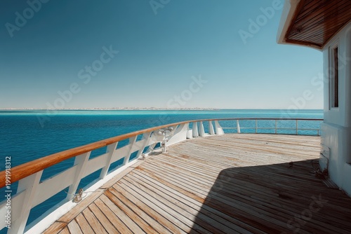 A deck on a ship overlooking serene blue water and a distant shoreline under a clear sky