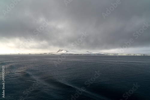 Antarctic expedition. View of snow-covered mountain and calm water under cloudy sky in a remote location during an overcast day. Antarctic Peninsula