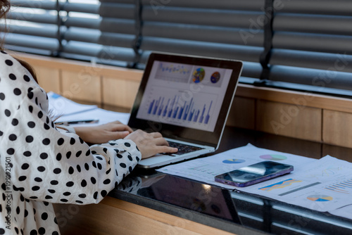 Smiling businesswoman working on laptop in café, enjoying hot drink, analyzing charts, planning projects, and staying connected in a modern professional lifestyle.
