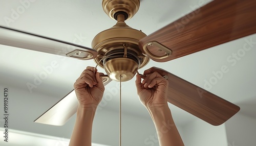 A person's hands reach up to pull the chain on a bronze ceiling fan.