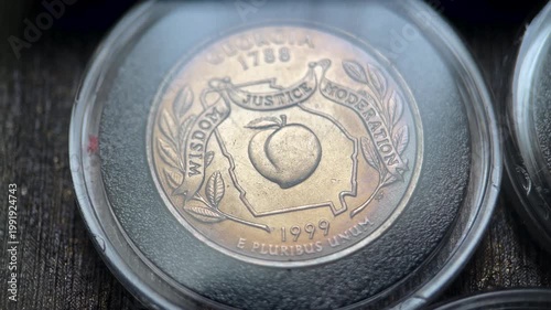 Close up video of a 1999 United States quarter dollar coin featuring the Georgia state reverse design with a peach, state outline, and the motto “Wisdom, Justice, Moderation.”