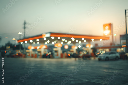 Blurred view of a gas station at dusk with illuminated lights and cars.