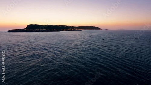Coastal landscape at sunset with a view of a distant island and calm ocean waters reflecting warm colors in the sky, creating a serene atmosphere for relaxation