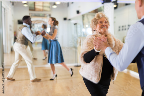 Man and elderly woman performing jazz dance in dancing room